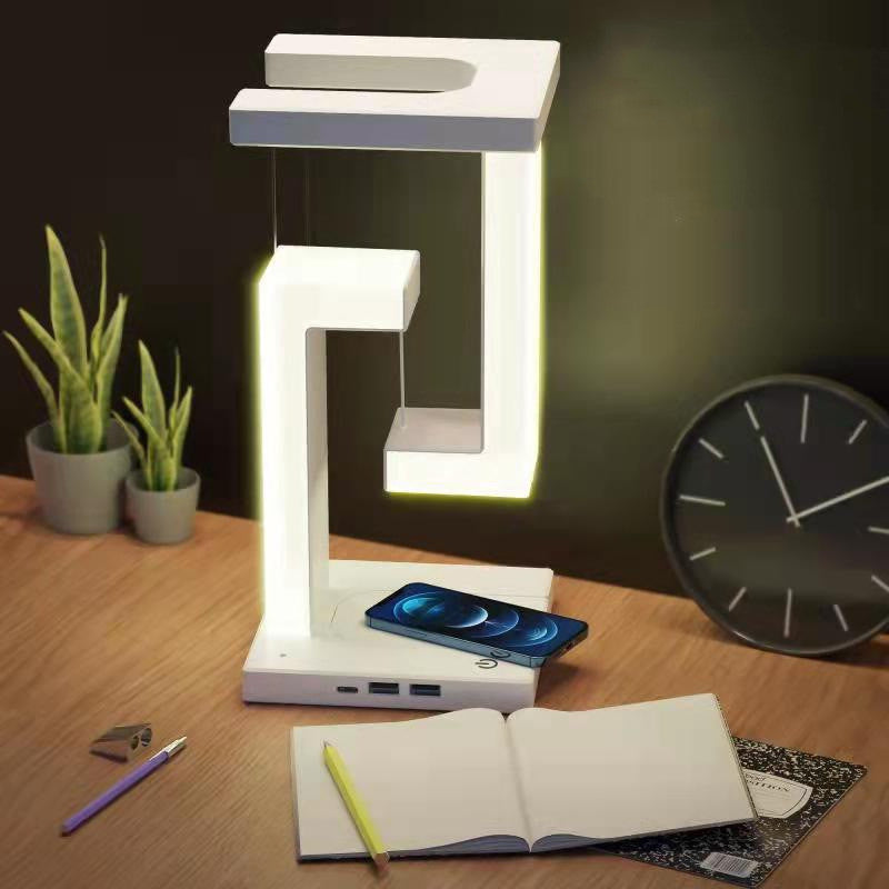 Levitating table lamp lit on desk with phone charging wirelessly